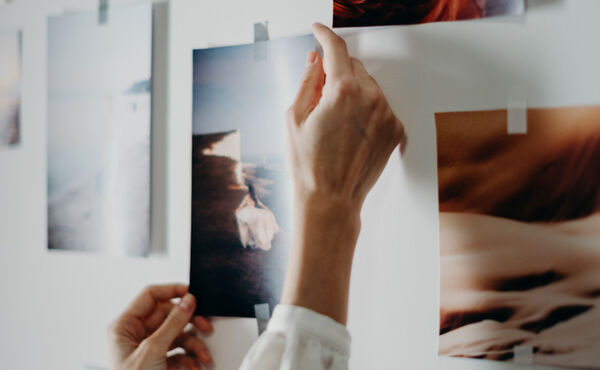 Hands taping inspirational photos to a wall vision board for a manifestation practice.